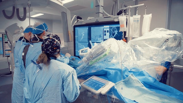 Une salle d'opération avec du personnel médical en pleine action, assistés par un bras robotisé.