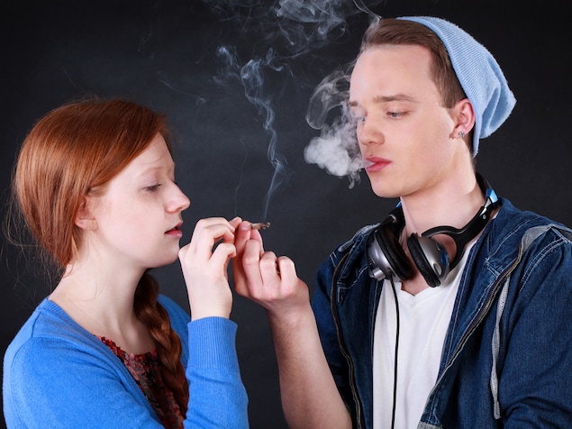 Une jeune fille et un jeune garçon échangent un joint de cannabis.