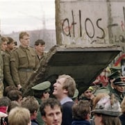 Des soldats sont debout sur un des panneaux tombés du mur de Berlin et regardent la foule massée tout près.