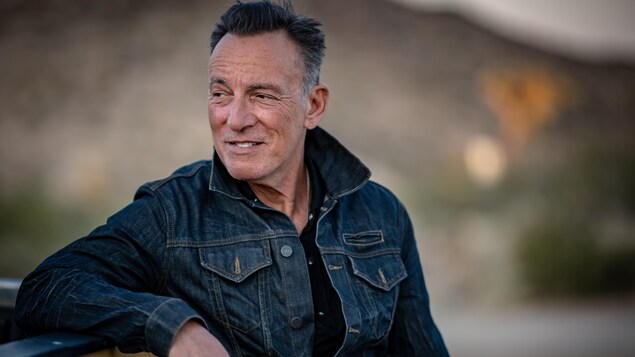 Bruce Springsteen sourit en regardant au loin.