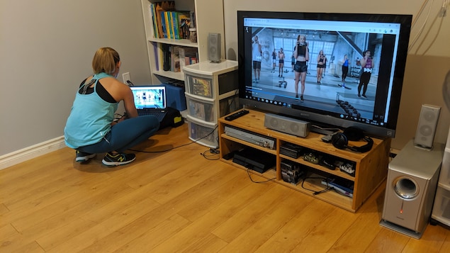 Une femme installe une vidéo de remise en forme sur son ordinateur, qui est connecté à un écran de télévision.