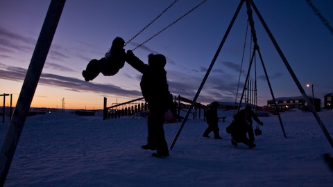 Des enfants jouent sur une balançoire à Iqaluit, au crépuscule.