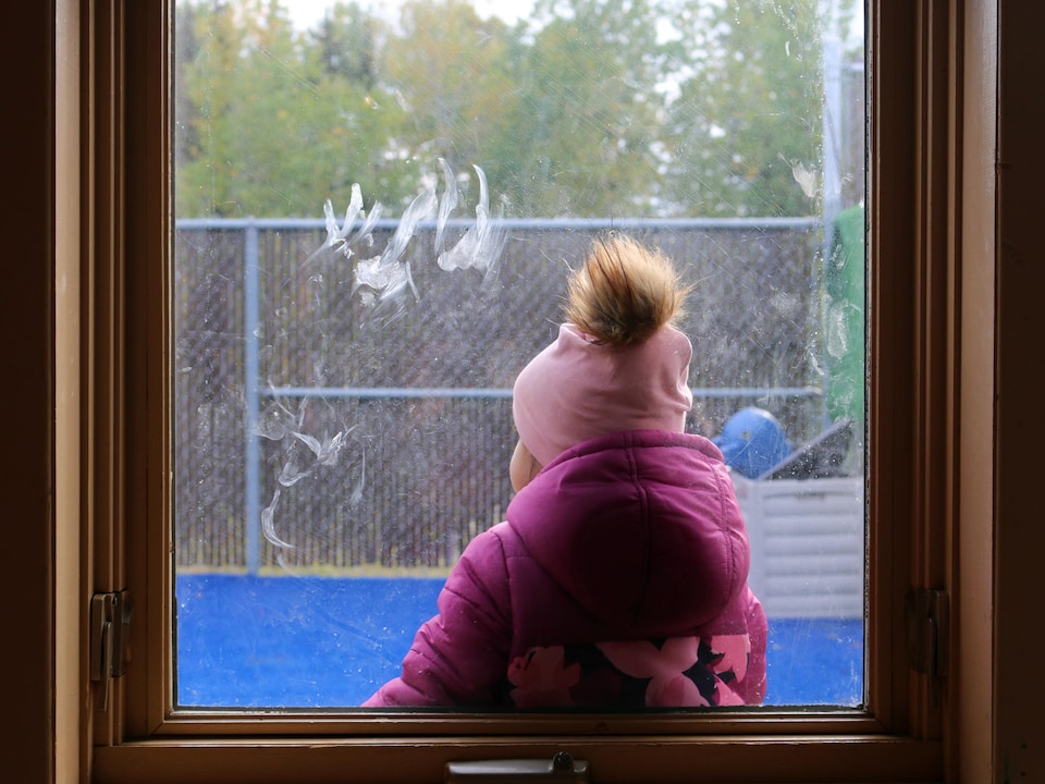 Un enfant dans un cour de garderie, à travers une fenêtre.