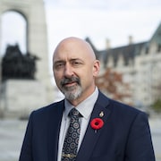 Alex Ruff devant le Monument commémoratif de guerre du Canada à Ottawa, alors qu'il porte un veston bleu et un coquelicot rouge. 