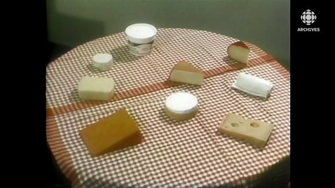 Des morceaux de fromage sont présentés sur une table ronde décorée d'une nappe Vichy.