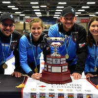 Les joueurs de curling prennent la pose devant un trophée.