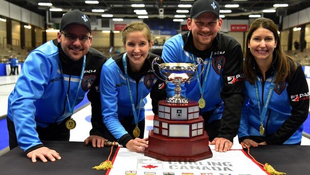 Les joueurs de curling prennent la pose devant un trophée.