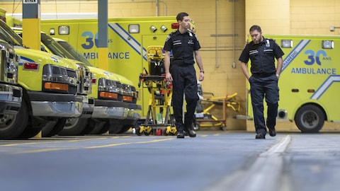 Marc-André Gaudreau et Mathieu Goyer marchent et discutent dans un garage d'ambulances.
