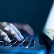 Un homme a les mains posées sur le clavier d'un ordinateur portable dans l'obscurité.
