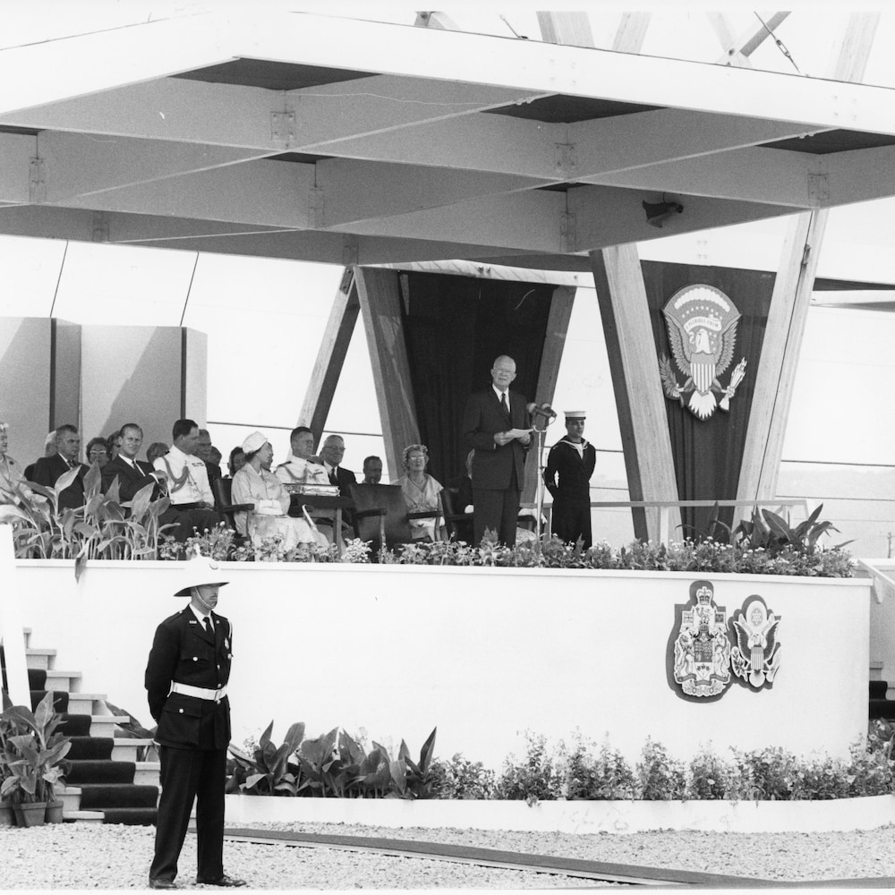 Le président américain Dwight Eisenhower offrant un discours sur la large tribune d'honneur où sont assis les autres dignitaires.