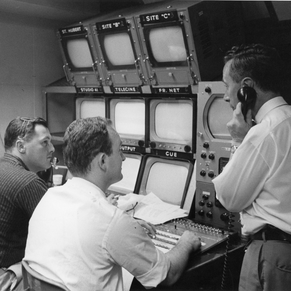 Des employés devant une rangée d'écran regardent un collègue qui parle dans un combiné de téléphone à cordon.