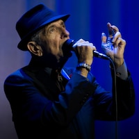 Leonard Cohen chante sur une scène au fond bleu. 