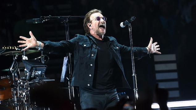 Le chanteur de U2, Bono, chante les bras écartés.