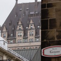Aperçu du toit du Château-Frontenac au travers de différents toits du Vieux-Québec. Une pancarte «Rue des Grisons» est installée sur un mur en pierre, en avant-plan. 