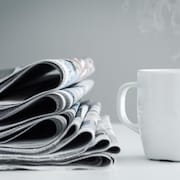 Une pile de journaux à côté d'une tasse de café.