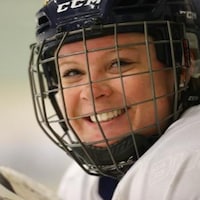 Une joueuse de hockey souriante porte un casque muni d'une grille.