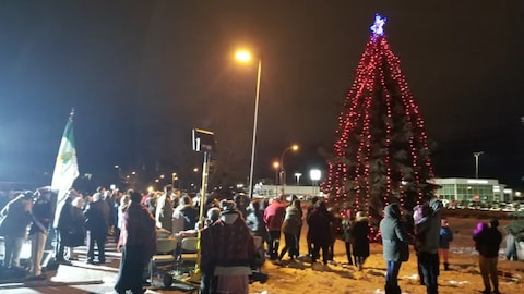 Un arbre géant avec des ampoules rouges et des gens rassemblés autour dehors. 