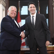Justin Trudeau et Doug Ford se serrent la main, souriants.