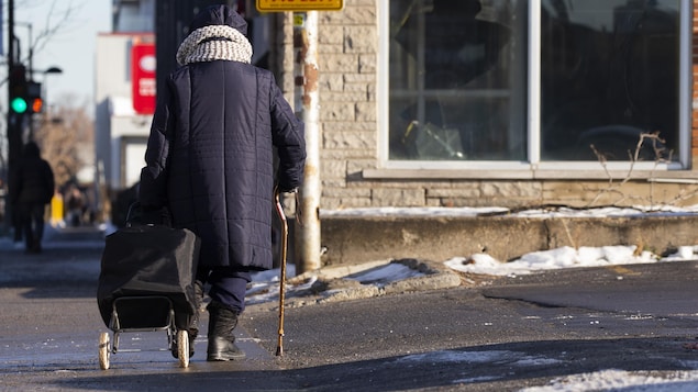 Une personne âgée avec une canne et tirant un chariot marche sur un trottoir de la rue Ontario à Montréal.