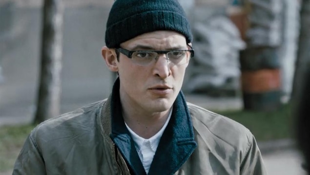 Un homme (Niels Schneider) portant un bonnet et des lunettes en plan moyen.