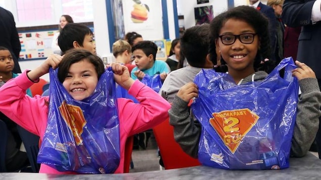 Des enfants montrent fièrement leur sac bleu avec la mention Breakfast2Go. 