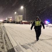 Un policier marche dans la neige devant des véhicules accidentés sur une autoroute.