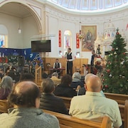Gens assis dans l'église avec un chanteur et un sapin de Noël.