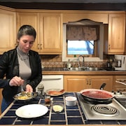 Le chef autochtone Lysanne O'Bomsawin est au comptoir d'une cuisine en train de mélanger de la nourriture dans un bol, alors qu'à ses côtés, des chaudrons sont sur les ronds d'une cuisinière, en attente.