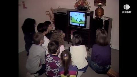 Un groupe d'enfants sont tournés vers un écran de téléviseur sur lequel se déroule une partie du jeu Mario Bros. sur console Nintendo.