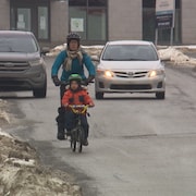 Une cycliste et son garçon partagent la route avec une voiture qui les suit de près