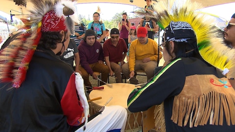 De jeunes autochtones encerclent un grand tambour sur lequel ils frappent