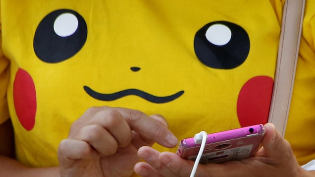 Une femme portant un chandail jaune à l'effigie de Pikachu utilise son téléphone cellulaire.