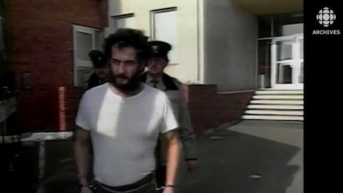 Allan Legere menotté et amené par deux policiers à son procès.