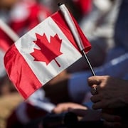 Une femme tient un drapeau canadien dans sa main. 