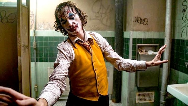 Dans une salle de bains sale et délabrée, un homme maquillé en clown interprété par Joaquin Phoenix esquisse un mouvement de danse.
