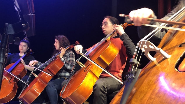 Quatre adolescents assis en demi-cercle jouent du violoncelle. 