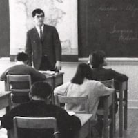 Un enseignant se tient debout devant une classe sur une photo d'archive usée et prise en noir et blanc.
