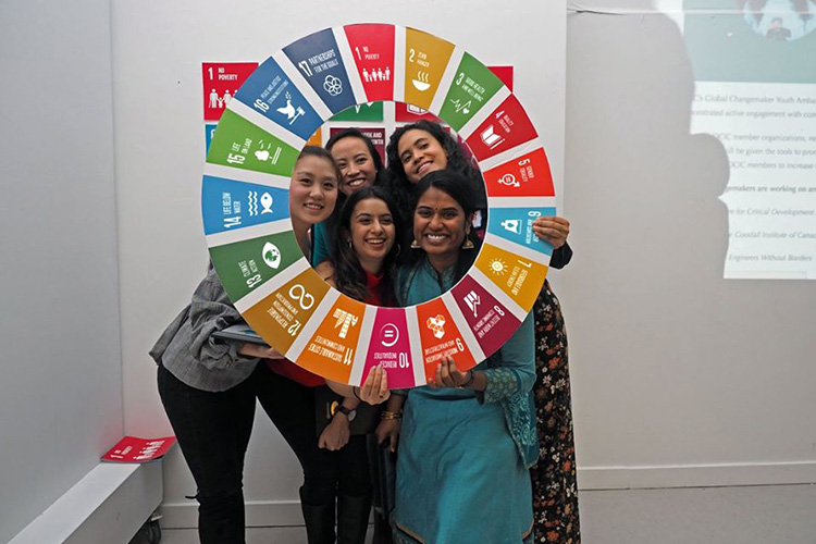A group of five smiling young women present at a gala hold a cardboard wheel representing the UN?s 2020 Agenda?s logo.