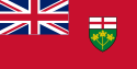 A red flag with a large Union Jack in the upper left corner and a shield in the center-right