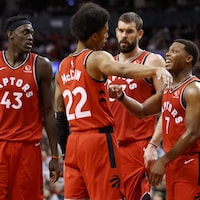 Deux joueurs discutent d'une stratégie tandis que deux autres prêtent l'oreille. Ils sont tous vêtus de l'uniforme rouge des Raptors de Toronto.