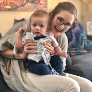 Jillian Schneider est assise sur un divan avec un bébé dans les bras.