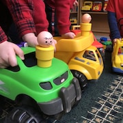Trois enfants non-identifiés d'âge préscolaire jouent ensemble avec des camions-jouets dans un service de garde.