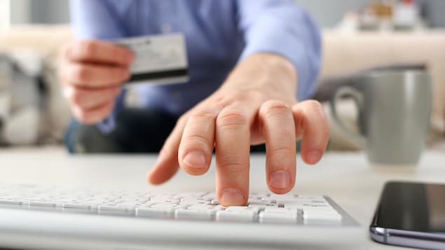 Une personne tient une carte de crédit en tapant sur son clavier.