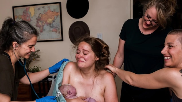 Une femme qui porte un nouveau-né dans ses bras est entourée de trois autres femmes.