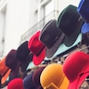 Plusieurs chapeaux de feutres disposés sur un support dans un marché extérieur.