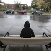 Un garçon est assis seul sur un banc au bord de la rue.