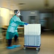 Une infirmière portant un masque et des habits de protection pousse un chariot dans le couloir d'un hôpital.