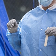 Un professionnel de la santé tient un écouvillon et une languette pour faire un test de dépistage.