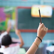 Plan serré de la main levée d'un enfant dans une classe qui tient un crayon.