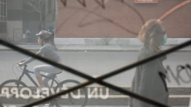 Une femme portant un masque et une cycliste circulent sur le Boulevard Maisonneuve, à Montréal